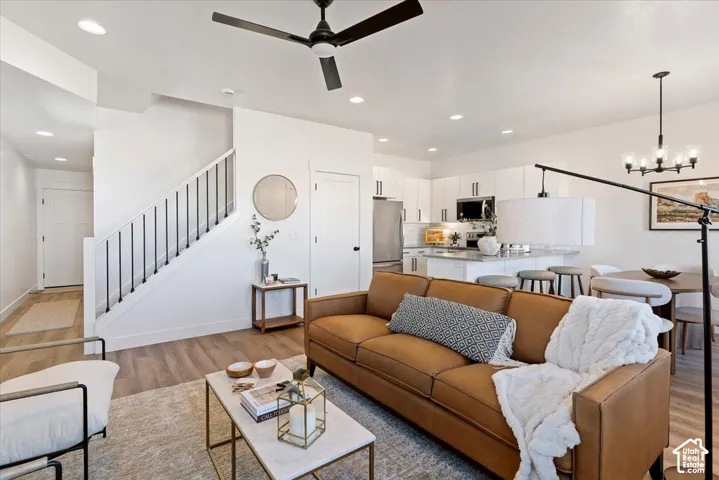 Open-concept interior featuring wood-finish flooring, recessed lighting, a modern staircase with a black metal railing, white cabinetry, and an integrated kitchen island