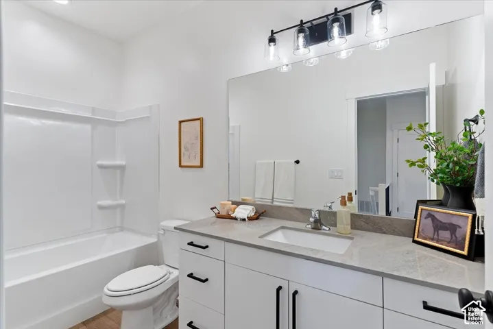 Bathroom featuring a vanity with stone-finish countertop and integrated sink, matte black hardware, large wall-mounted mirror, four-light vanity fixture, and a white tub-shower combination