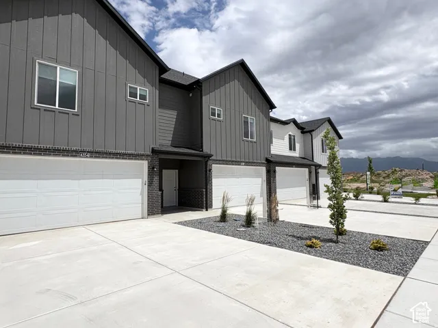 Modern vertical board-and-batten siding with dark brick masonry accents, attached multi-car garages, and concrete driveway paving