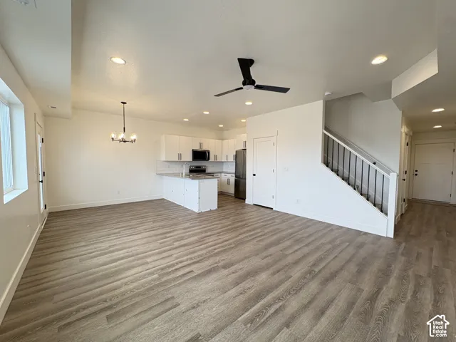 Open-concept area featuring wood-finish flooring, white cabinetry, a kitchen island, recessed lighting, and a staircase with metal balusters