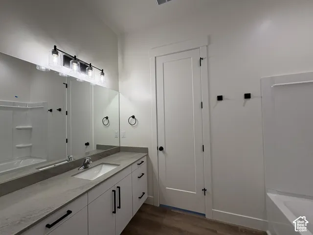 Bathroom vanity featuring white cabinetry, stone-finish countertop with an integrated sink, matte black hardware, a full-width mirror, and a four-light vanity fixture