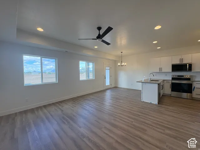 Open floor plan featuring wood-finish flooring, recessed lighting, matte black ceiling fan, white cabinetry, and stainless steel appliances
