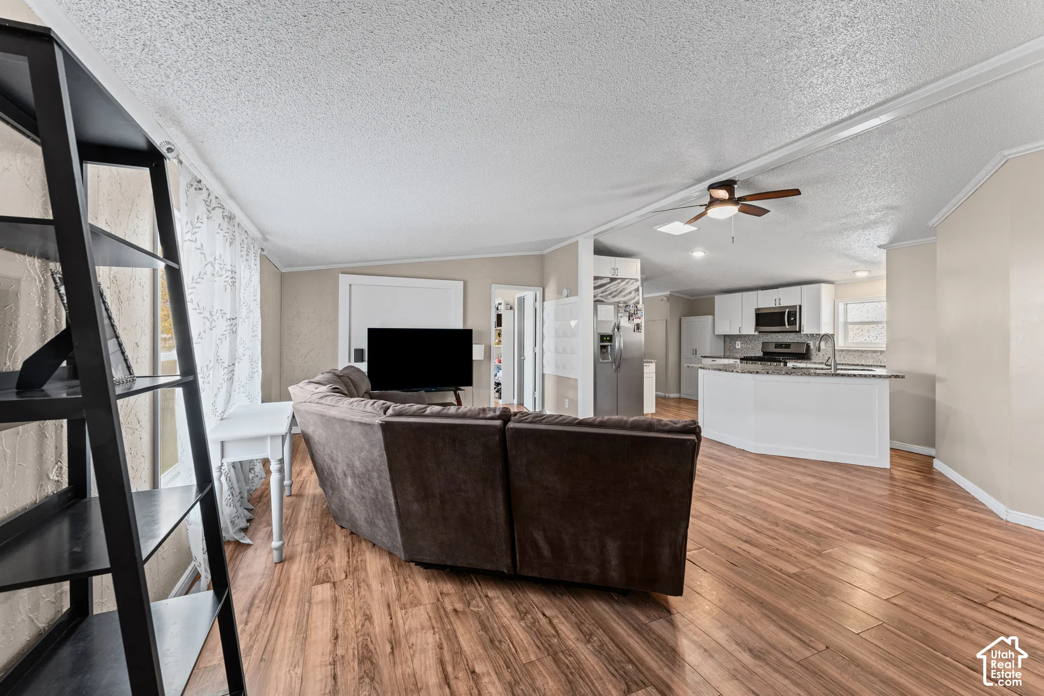 Open floor plan featuring wood-finish flooring, recessed lighting, ceiling fan, and a kitchen island with stone-finish countertops and white cabinetry