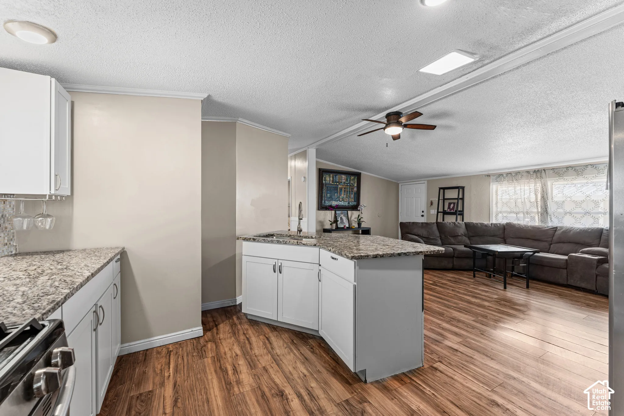 Kitchen featuring white cabinetry, stone-finish countertops, an integrated island, stainless steel appliance, and wood-finish flooring