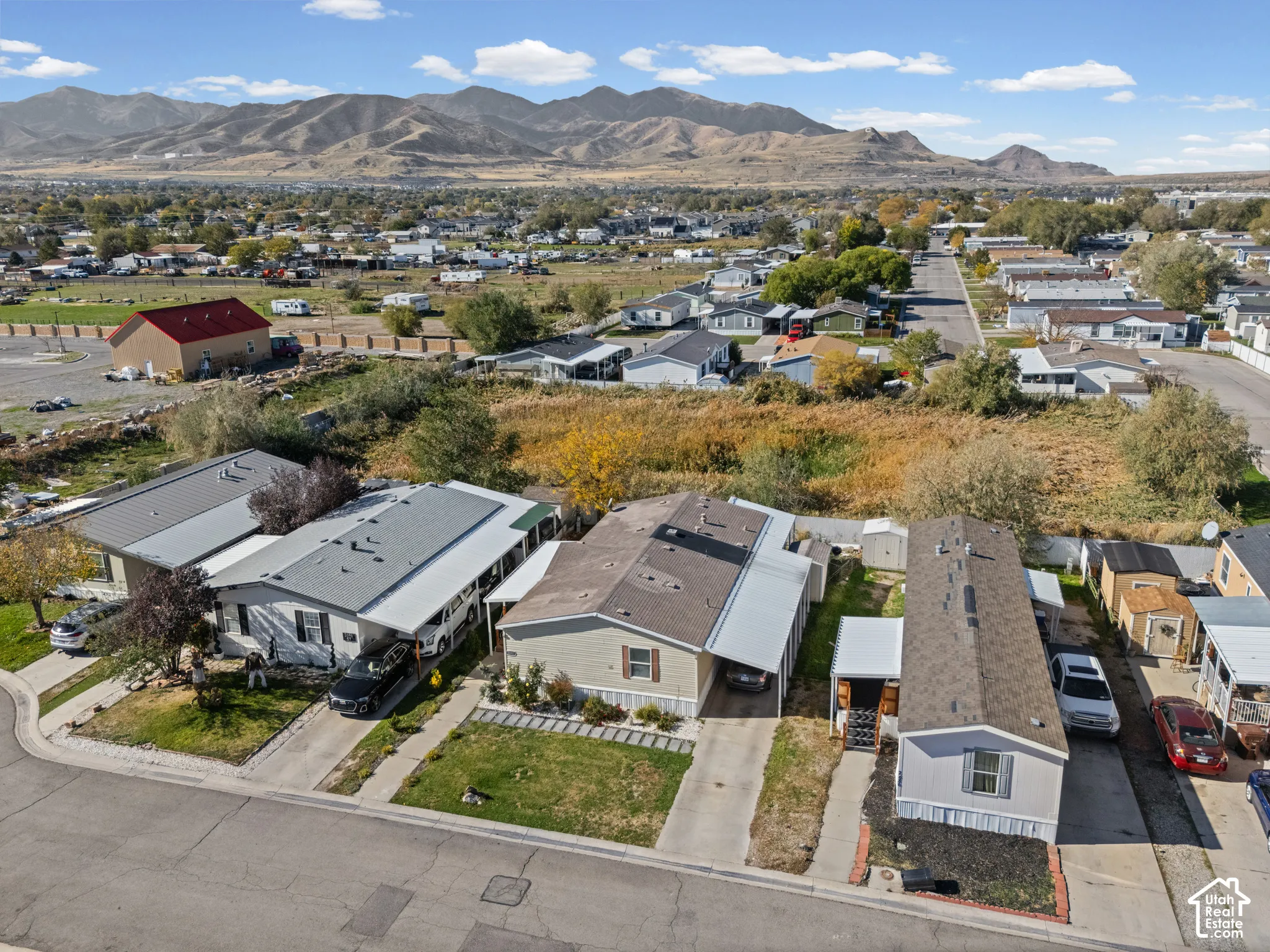 Aerial perspective featuring residential structures with attached metal carports, concrete driveways, and mountain range backdrop