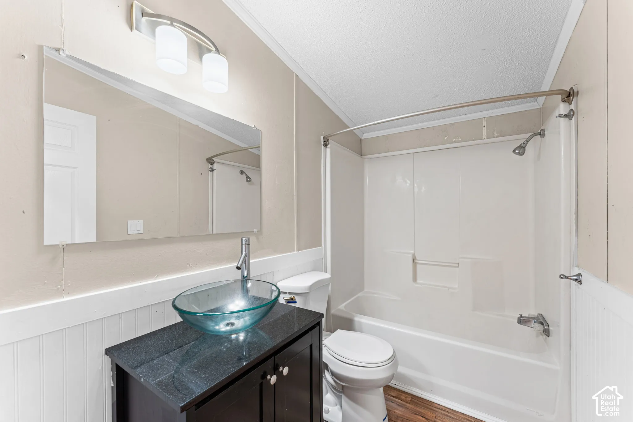 Vanity featuring a dark cabinetry base, stone-finish countertop, and glass vessel sink with a metal faucet, paired with a white-finish tub-shower combination, wall-mounted mirror, and two-light fixture