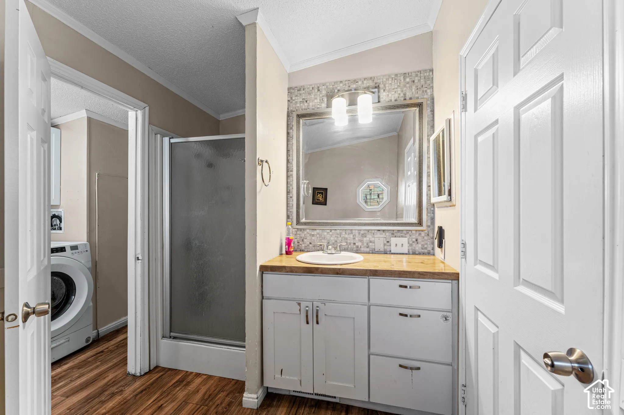 Bathroom featuring a wooden countertop vanity, integrated circular basin, textured tile backsplash, framed wall mirror, and a walk-in shower with frosted glass door
