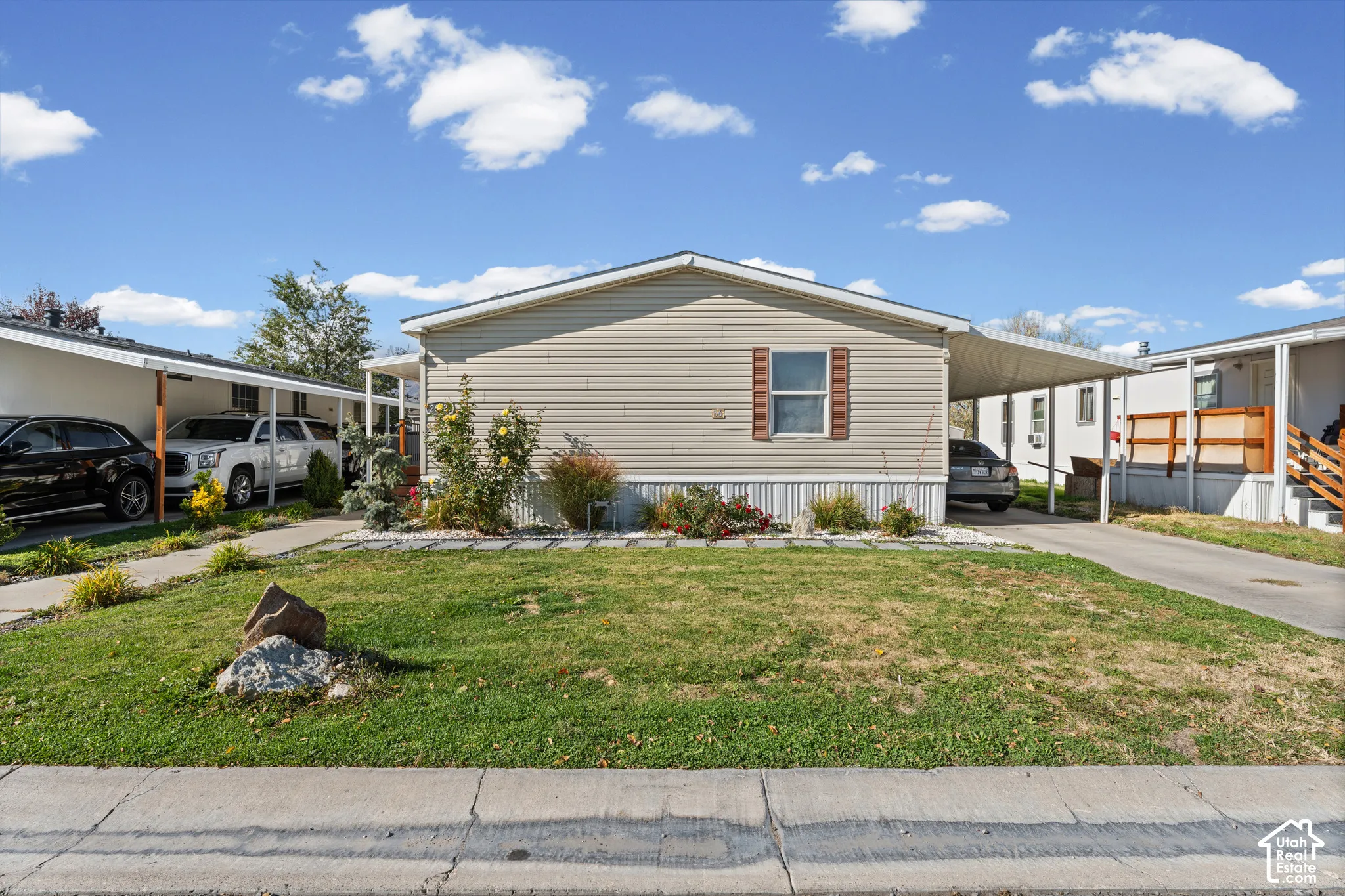 Exterior featuring light-toned horizontal siding, a covered carport, manicured lawn with low-maintenance landscaping, and decorative shutters