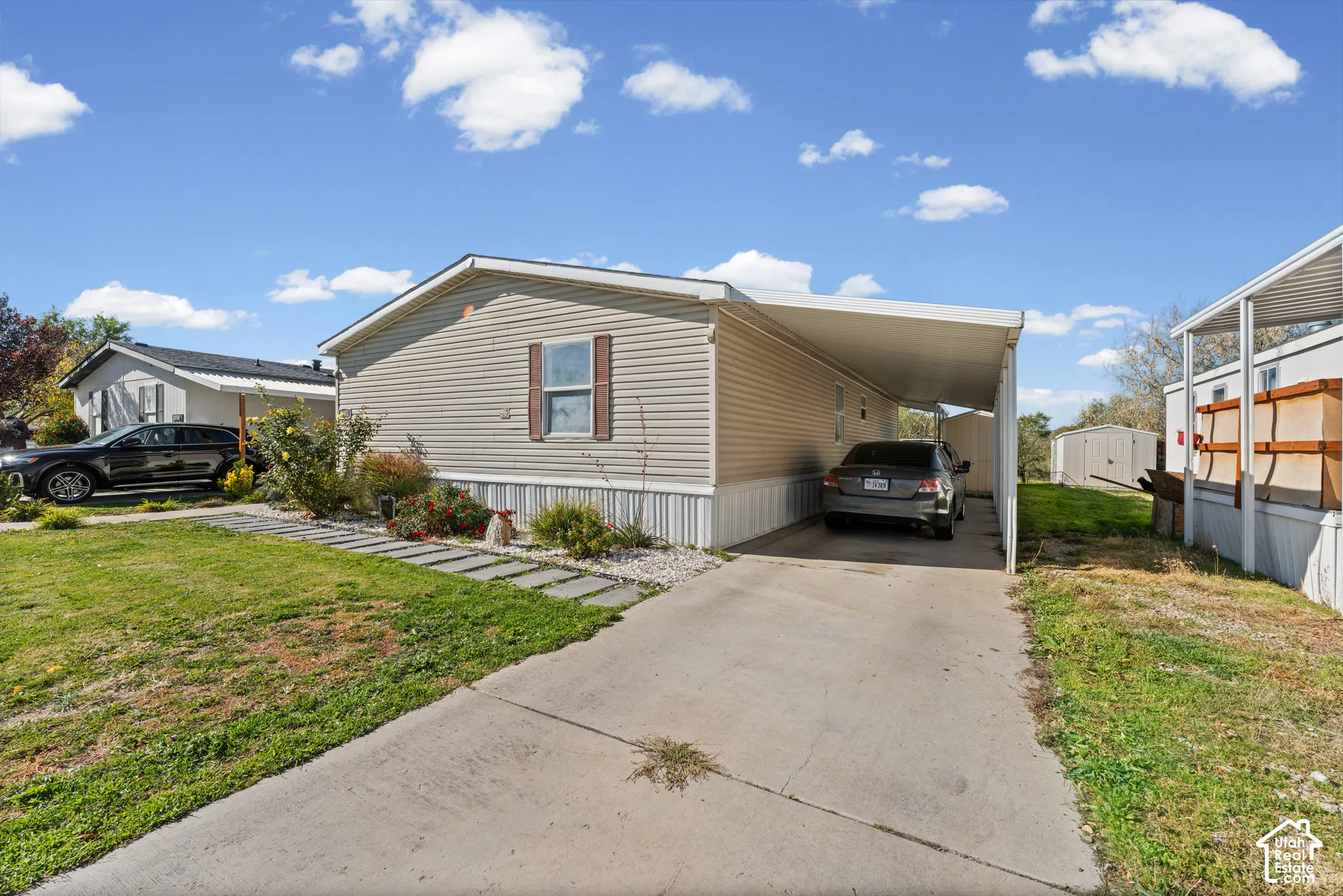 Exterior facade featuring light-toned horizontal siding, a concrete driveway, a covered carport, and a stone walkway