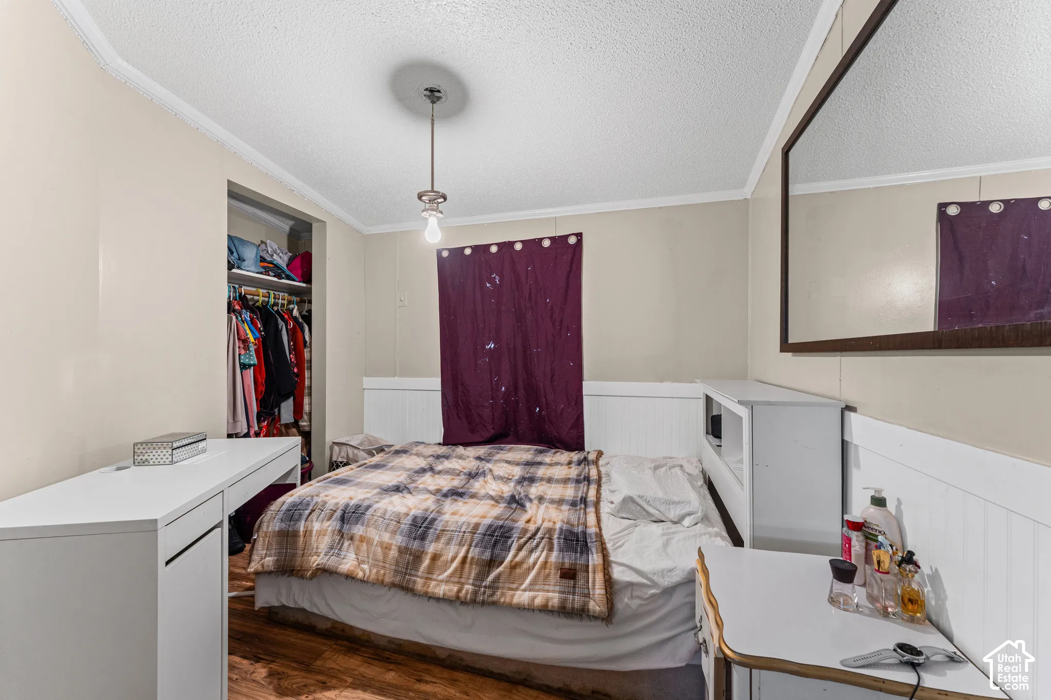 Room featuring wood-finish flooring, white wainscoting, an integrated wall-mounted mirror, and a ceiling-mounted pendant light