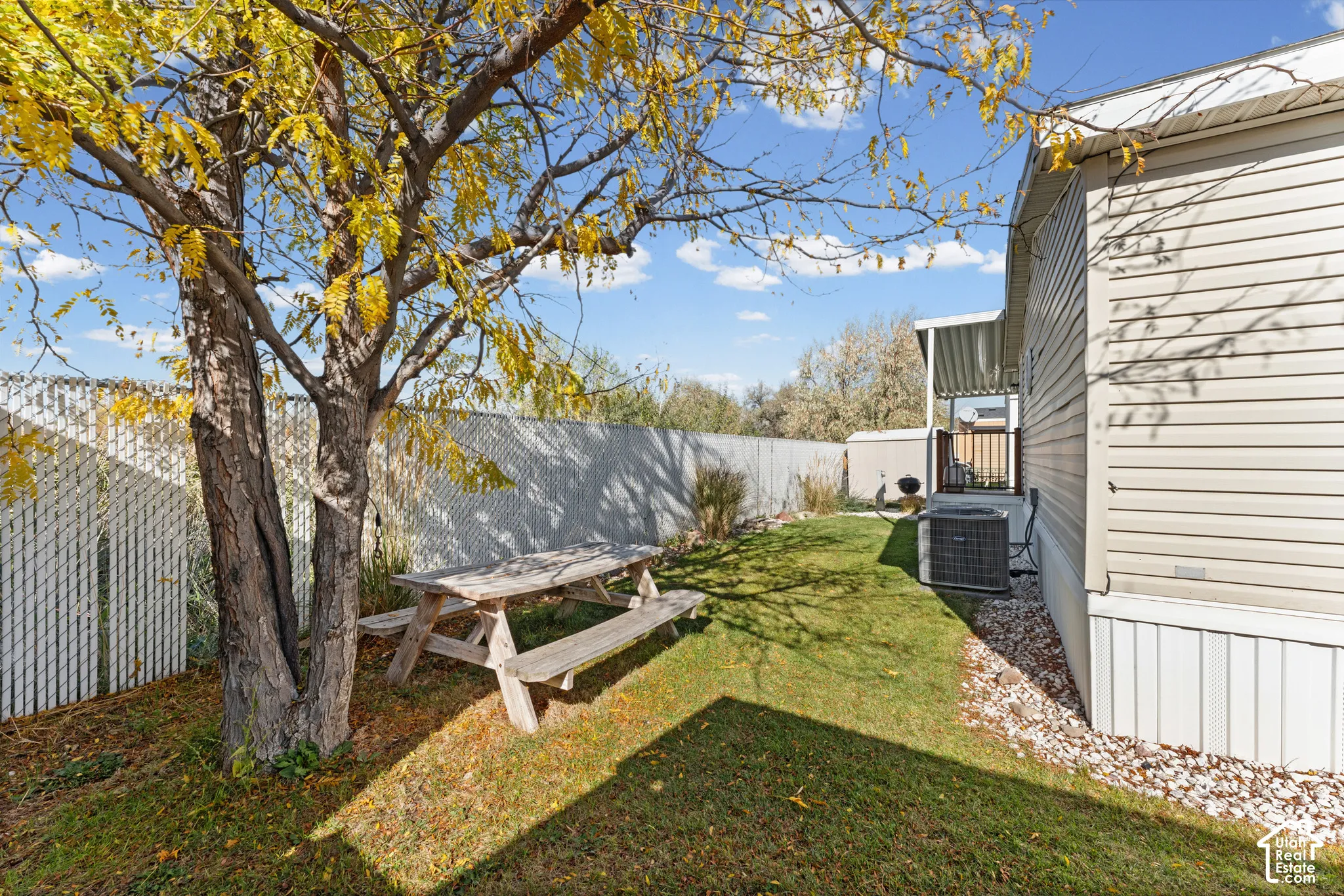 Side yard featuring vinyl siding, white chain-link fencing, a mature tree, and a rock-landscaped border