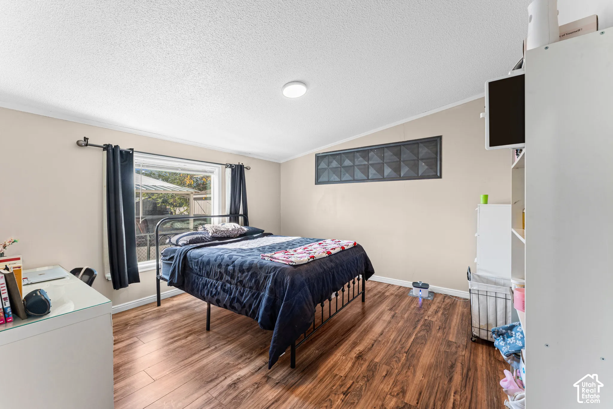 Bedroom featuring wood-finish flooring, a large window, a decorative geometric-patterned wall inset, and a flush-mount ceiling light