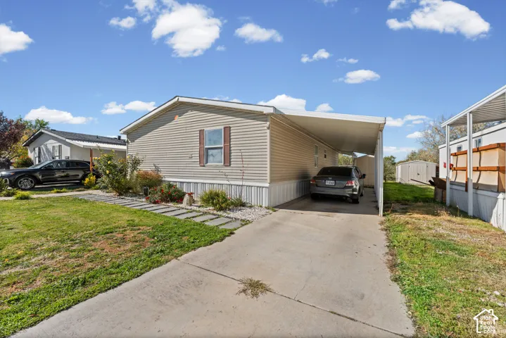 Exterior facade featuring light-toned horizontal siding, a concrete driveway, a covered carport, and a stone walkway