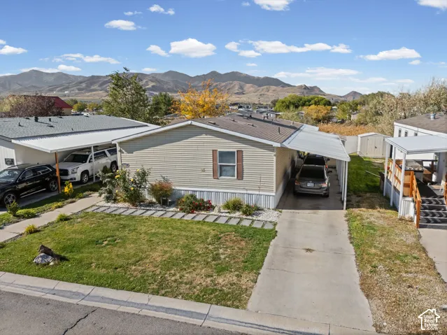 Exterior featuring horizontal siding, a private concrete driveway, two metal-frame covered parking structures, and a backdrop of mountain scenery