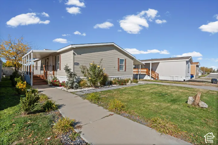 Vinyl siding exterior featuring a covered front porch, concrete walkway, and landscaped garden beds