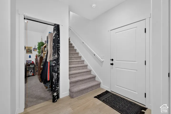 Entryway featuring wood-finish flooring, a white panel front door with matte black hardware, and a carpeted staircase with a white handrail