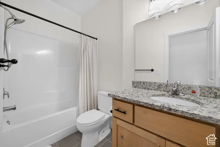 Bathroom featuring a vanity with stone-finish countertop, undermount sink, and matte black hardware, paired with a shower-tub combination and tile flooring