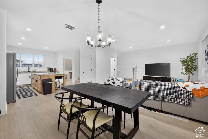Open-concept living space featuring wood-finish flooring, recessed lighting, a five-light chandelier, and kitchen island cabinetry with a stone-surface countertop