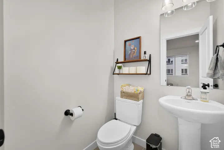 White pedestal sink with chrome faucet, frameless wall-mounted mirror, matte black hardware, and three-light glass fixture