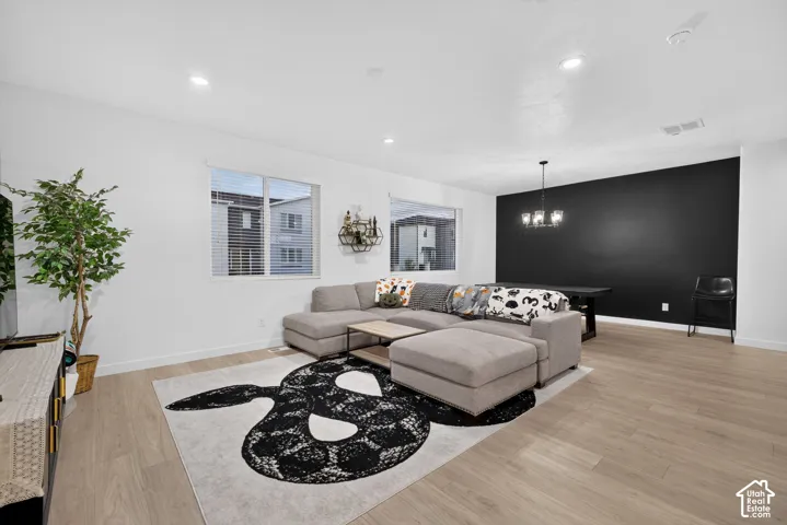 Open-concept interior featuring light wood-finish flooring, recessed lighting, a statement black accent wall, and a multi-arm chandelier