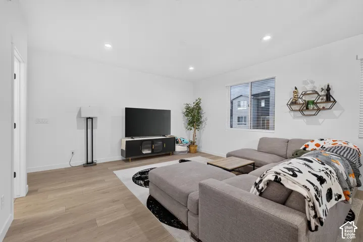Neutral-toned living space featuring light wood-finish flooring, recessed ceiling lighting, and a single-pane window