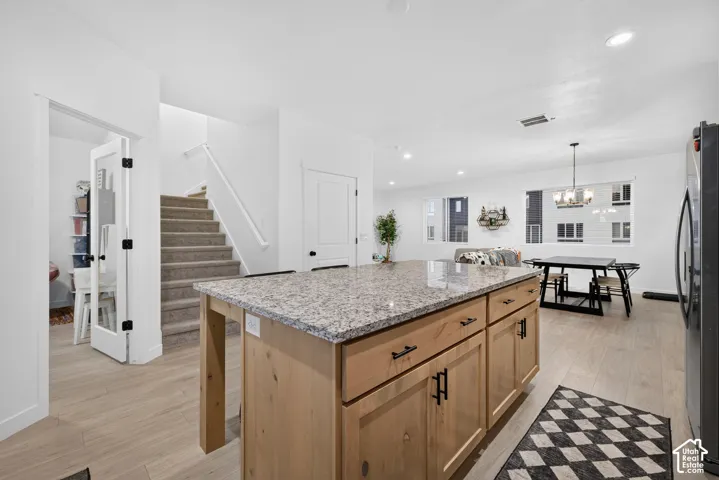 Kitchen featuring a central island with natural wood-finish cabinetry, stone-look countertop, recessed ceiling lighting, and wood-finish flooring