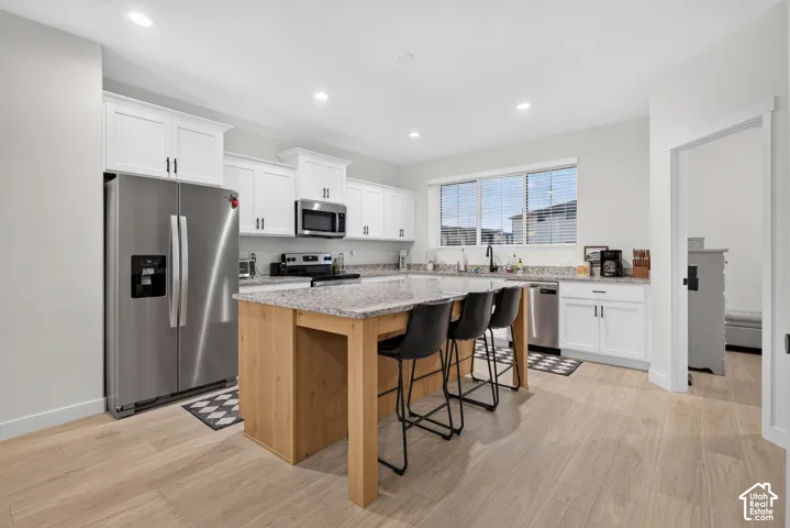 Kitchen featuring white shaker-style cabinetry, stone countertops, a wood-finish island with integrated seating, recessed lighting, and stainless steel appliances