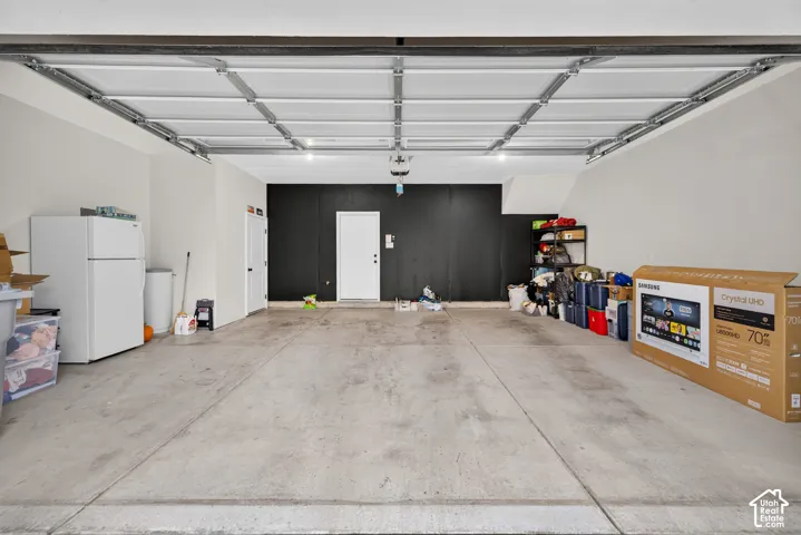 Attached garage featuring a concrete floor, high-clearance overhead door, and dedicated utility access door
