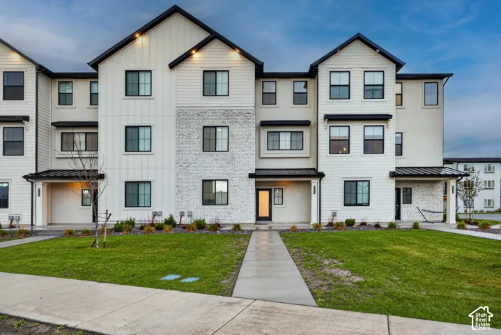 Modern exterior featuring white vertical siding and brick masonry accents, black-framed windows, multi-gabled rooflines, and a concrete walkway