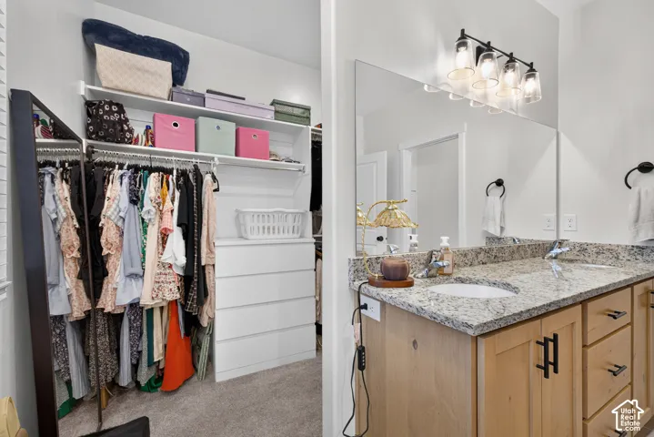 Bathroom featuring a dual-sink vanity with stone-finish countertops, light-toned wood cabinetry, and a full-width mirror with four-light fixture