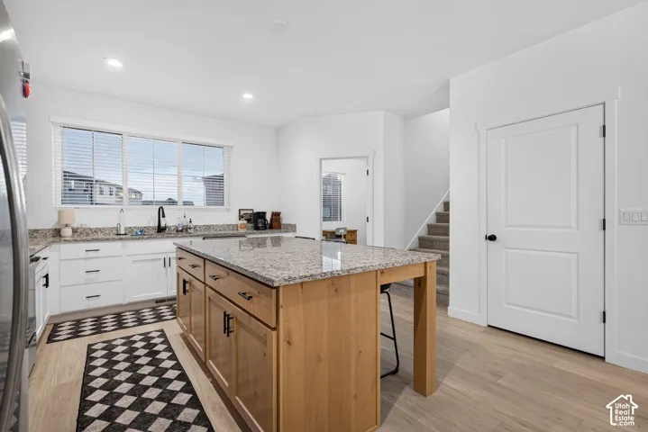 Kitchen featuring stone-finish countertops, a wood-finish island with seating space, white shaker-style cabinetry, matte black hardware, and wood-finish flooring