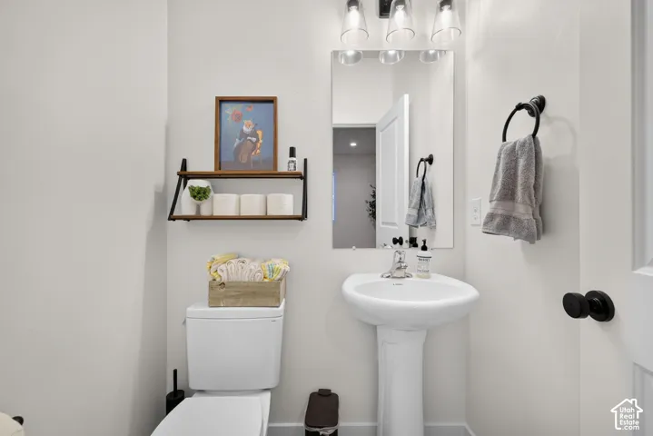 Pedestal sink with chrome faucet, frameless wall mirror, three-light vanity fixture, and matte black hardware