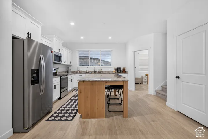 Kitchen featuring white shaker-style cabinetry, wood-finish kitchen island with stone countertop, stainless steel appliances, and wood-finish flooring