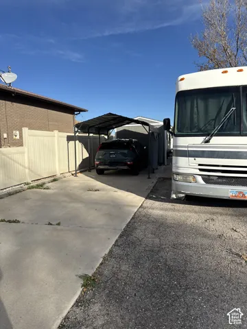 Concrete driveway with metal-framed carport, enclosed by vinyl privacy fencing