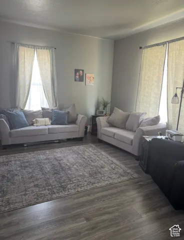 Living area featuring wood-finish flooring and two windows with rod-mounted curtains