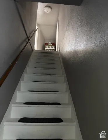 Staircase featuring white risers and treads, dark textured stair treads, and a wall-mounted wooden handrail