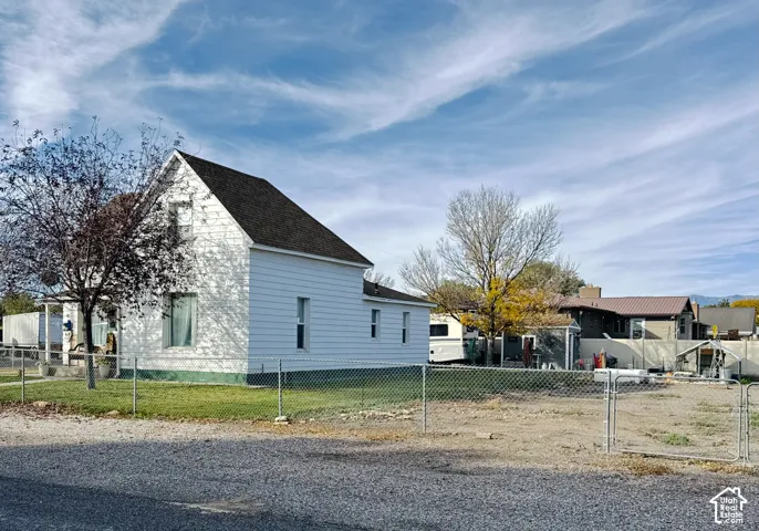 Two-story residence featuring white horizontal siding, an asphalt shingle roof, and a perimeter chain-link fence on a gravel-surfaced lot
