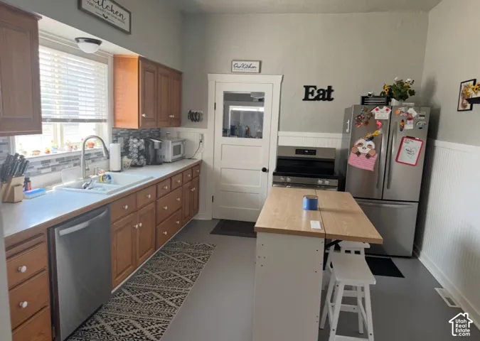 Kitchen featuring wooden cabinetry, white-toned countertops, a stainless steel dishwasher, a multi-pane glass-panel door, and white beadboard wainscoting