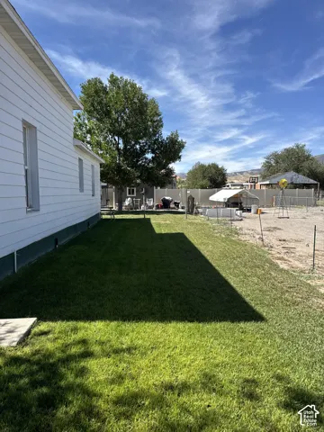 Exterior grounds featuring white horizontal siding, a fenced perimeter, expansive lawn area, gravel surface, and mature trees
