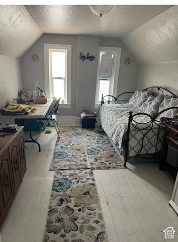 Room featuring sloped ceilings, painted wood-finish flooring, two double-hung windows with white casing, and a dome-style flush mount ceiling light