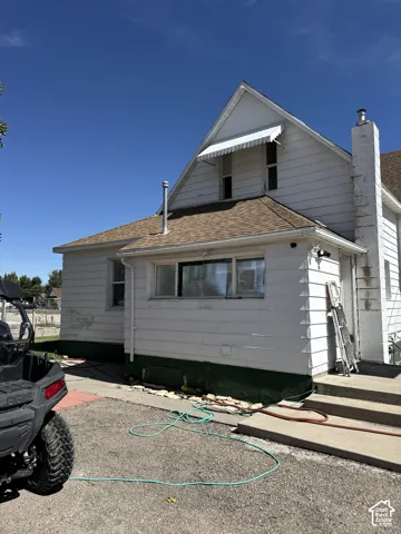 Exterior featuring white lap siding, a steeply pitched roofline, an external masonry chimney, and a metal window awning
