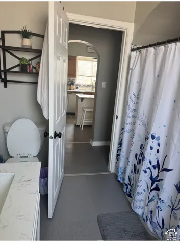 Bathroom featuring a vanity with a white-veined countertop, wall-mounted metal shelving, a tub-shower combination with an arched doorway, and solid-surface flooring