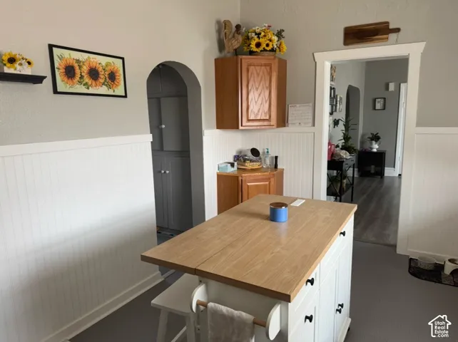 Kitchen featuring white beadboard wainscoting, arched doorway, and built-in wood-finish cabinetry