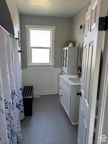 Bathroom featuring a white vanity with a stone countertop, built-in vertical cabinetry, wainscoting, and a single-hung window with decorative trim