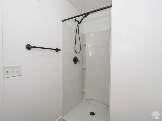 Shower enclosure featuring integrated shelving, a matte black handheld shower head, and matching matte black towel bar
