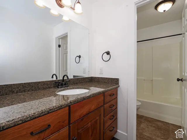 Bathroom featuring knotty alder cabinetry with a granite countertop, undermount sink, oil-rubbed bronze faucet, full-width vanity mirror, and a tub-shower combination
