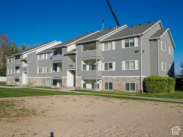 Multi-story exterior featuring gray stucco facade, stone veneer foundation, and manicured landscaping