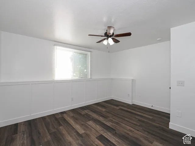 Interior space featuring wood-finish flooring, white board-and-batten wainscoting, a single-pane window with horizontal blinds, and an attached multi-light ceiling fan