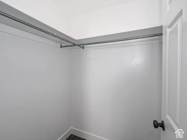 Storage space featuring neutral painted walls, multi-level metal hanging rods, and dark wood-finish flooring