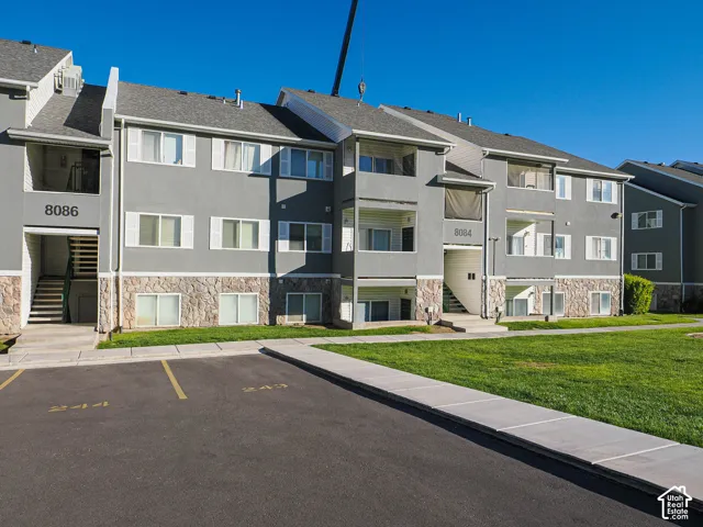 Gray stucco exterior with stone veneer foundation, paved parking, and well-maintained community grounds